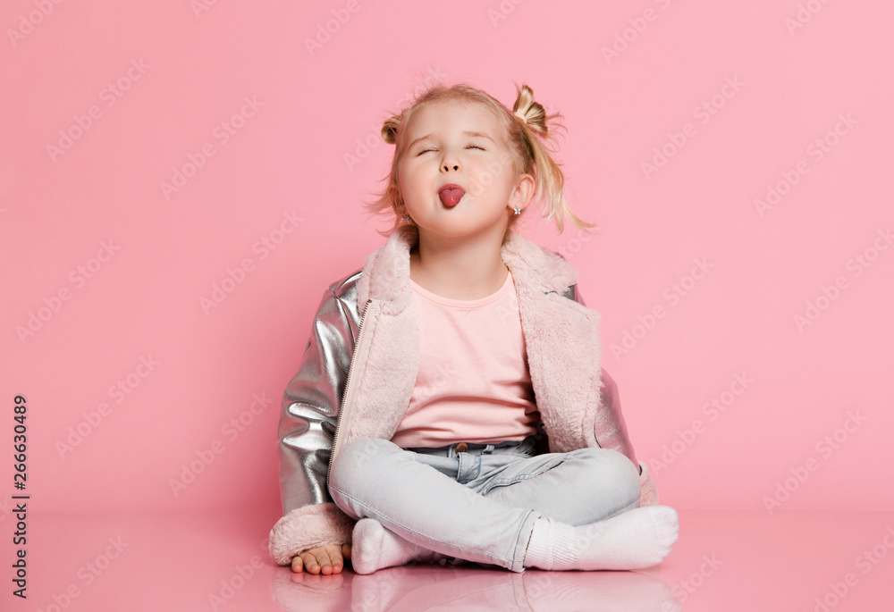 Portrait of a little girl in stylish clothing sitting on pink background and playing up Portrait of a little girl in stylish clothing sitting on pink background and playing up