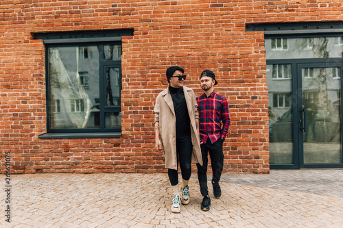 Gay couple walking around the city against a brick building holding hands © pantovich