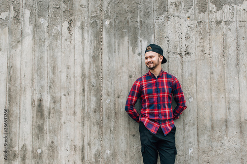 bearded man in a plaid shirt leaning against a gray wall standing in the open air © pantovich