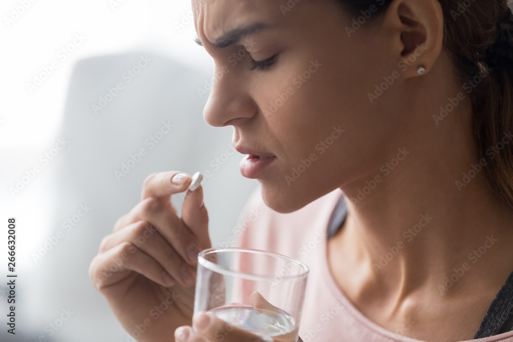 Closeup of frown woman holding pill and glass of water Closeup of frown woman holding pill and glass of water