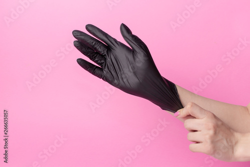 hand black gloves of doctor or hair stylist on pink background. gloves are worn on the arm