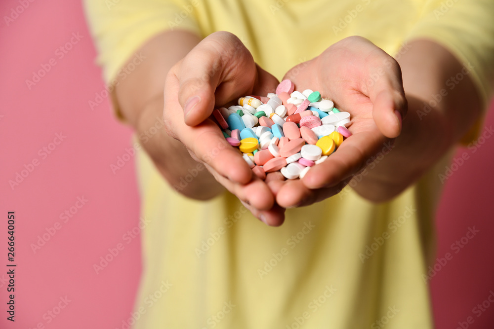 A handsome man in T-shirt on a pink background holding pills in his hand A handsome man in T-shirt on a pink background holding pills in his hand