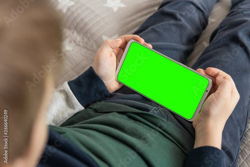 Phone a for keying is holding kid. Smartphone with a green screen in hand child . Smartphone with a hromakey in the hands of a child top view close up. photo