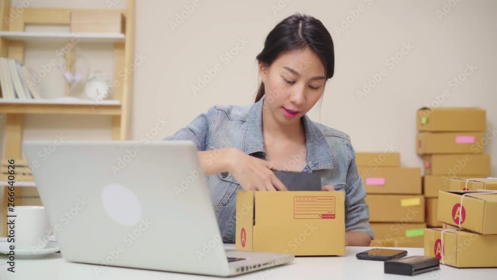 Beautiful smart Asian young entrepreneur business woman owner of SME online checking product on stock and packing put on the boxes working at home. Small business owner at home office concept. Beautiful smart Asian young entrepreneur business woman owner of SME online checking product on stock and packing put on the boxes working at home. Small business owner at home office concept.
