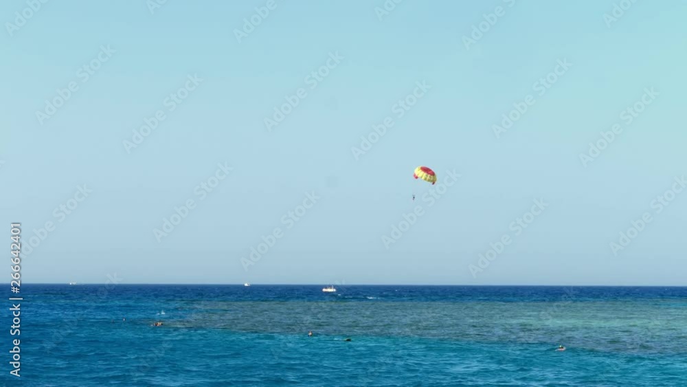 Parachute from kitesurfing hovers over the water's edge against the clear blue sky. summer, seascape. water surface, quiet calm turquoise sea and blue sky. vacationers swim with masks for snorkeling Parachute from kitesurfing hovers over the water's edge against the clear blue sky. summer, seascape. water surface, quiet calm turquoise sea and blue sky. vacationers swim with masks for snorkeling
