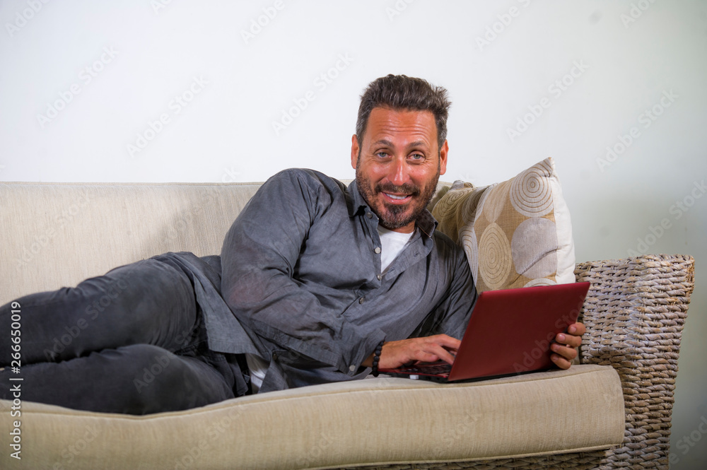 natural lifestyle portrait of young handsome and successful self employed man working at home using laptop computer lying relaxed at living couch networking
