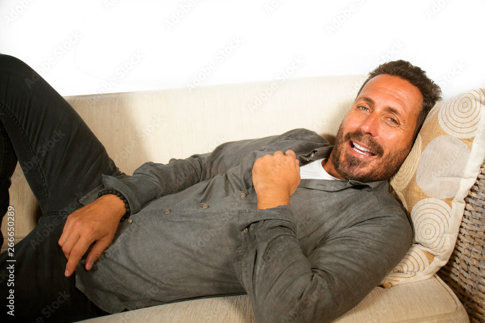 Fototapeta premium lifestyle home portrait of young attractive and happy white man with beard and casual shirt lying relaxed and cozy at living room sofa couch resting and smiling cheerful