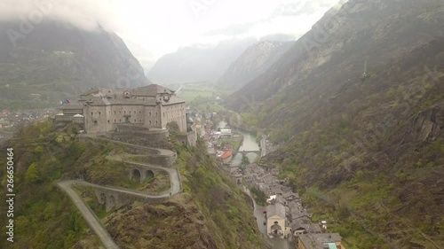 Moody aerial view Aosta Valley, northwestern Italy. Drone flies forward overlooking historical Forte di Bard. Beautiful cloudy wet rainy overcast alp landscape.