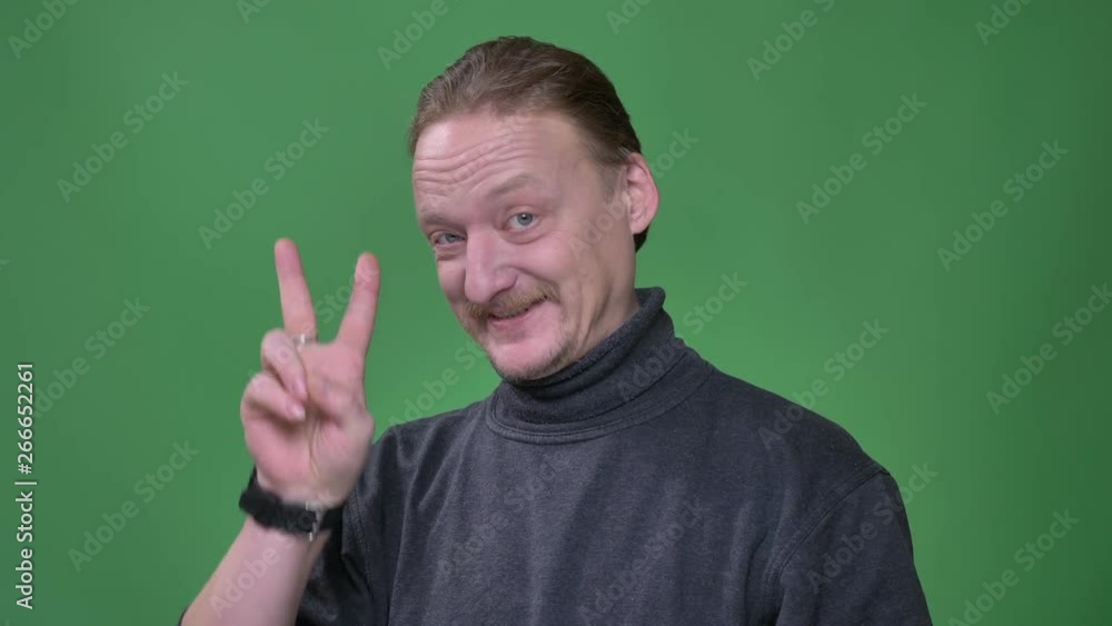 Portrait of middle-aged man with beard gesturing piece sign to demonstrate everything is fine on green background. Portrait of middle-aged man with beard gesturing piece sign to demonstrate everything is fine on green background.