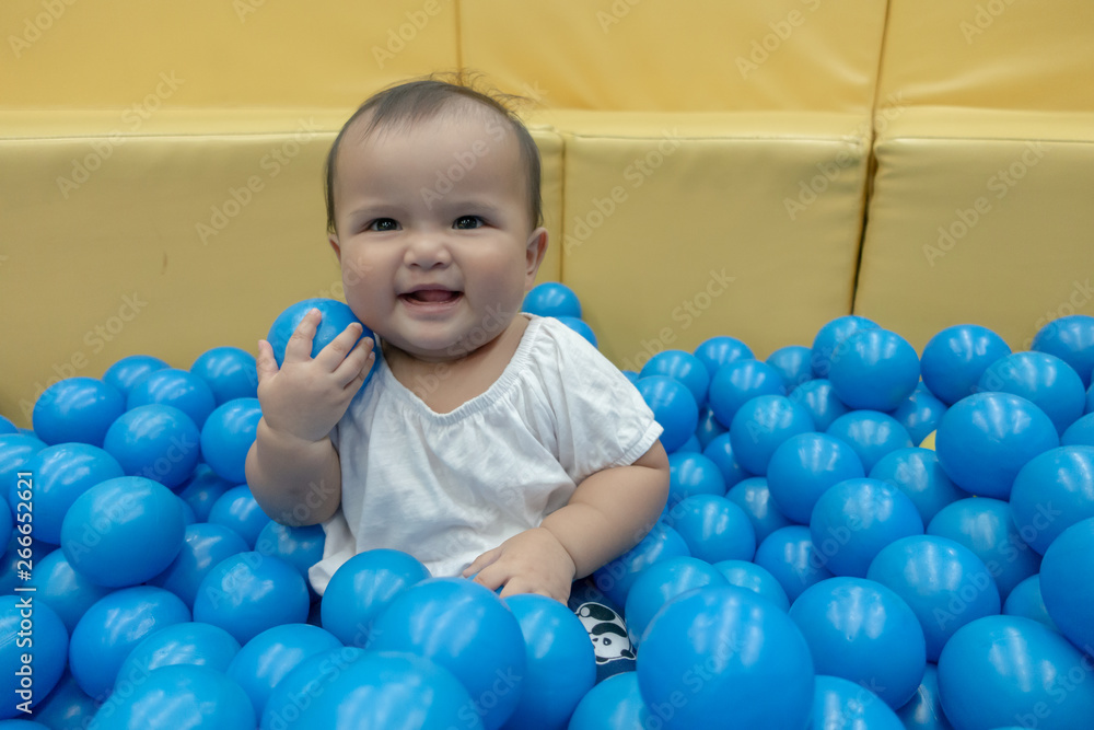 Obraz premium Happy Asian baby girl playing in a big dry pond full with blue plastic balls