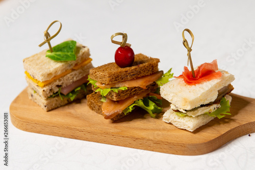 Three small sandwiches on a cutting board in the interiors of the restaurant. Cold appetizers.