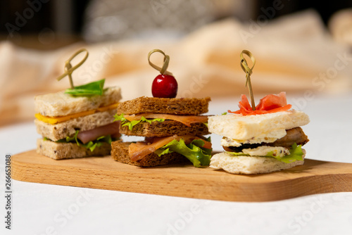 Three small sandwiches on a cutting board in the interiors of the restaurant. Cold appetizers.