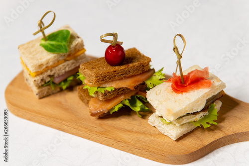 Three small sandwiches on a cutting board in the interiors of the restaurant. Cold appetizers.