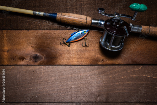 A vintage fishing rod and reel, with a lure on a wooden plank background with copy space