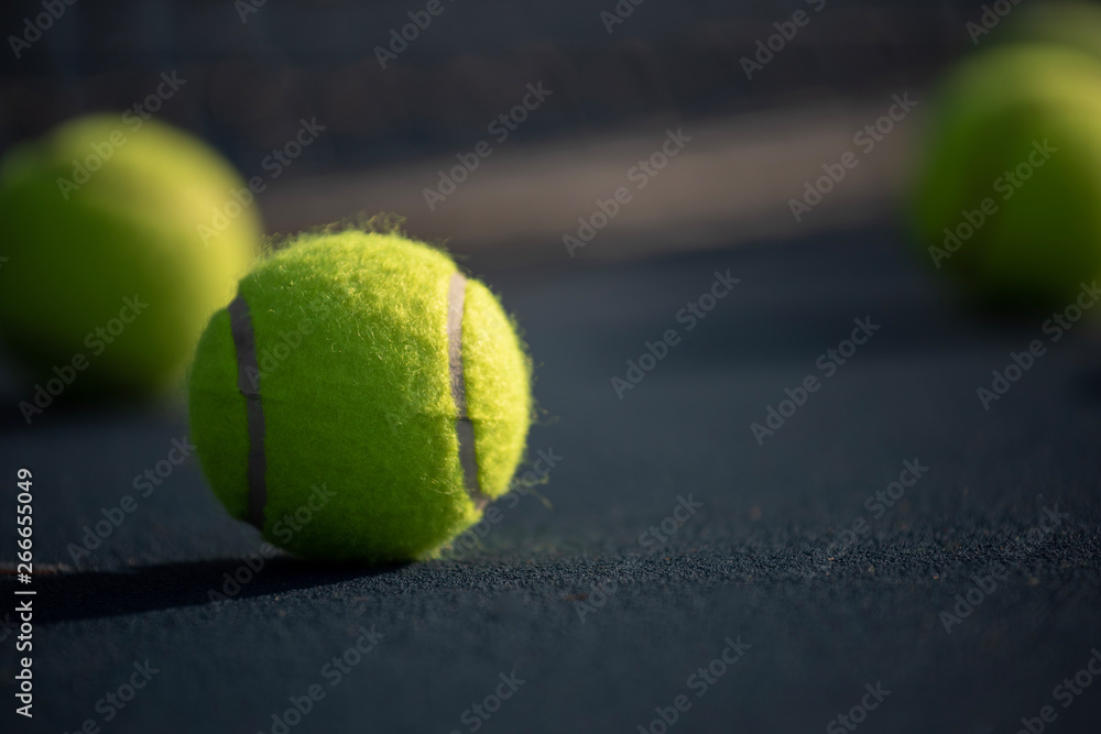 A group of yellow tennis ball on a court with net in background. Sports or exercise background.
