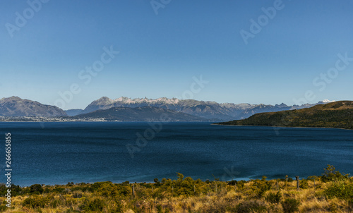 Colorful nature scenic photo of transparent aquamarine blue water surface of a lake with forest and Andes mountains in Patagonia, Argentina