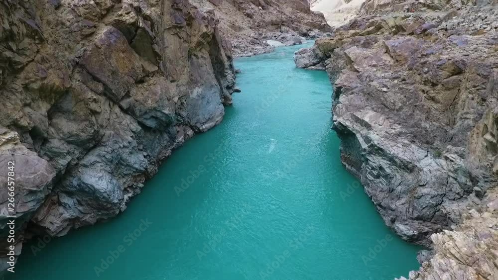 Drone, exterior, pushing in, medium wide shot of a blue river running through mountainous cliffs. Drone, exterior, pushing in, medium wide shot of a blue river running through mountainous cliffs.