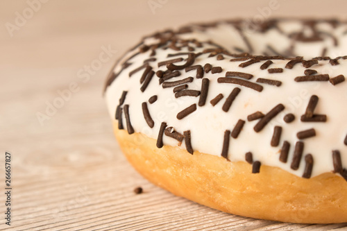 Fresh glazed donut with chocolate sprinkles on a wooden table.