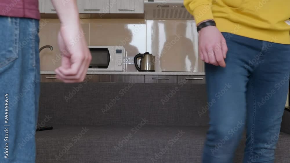 Two men are walking around the room. Young guys come up to the sofa, then turn around and leave. A kitchen on the background. 4K footage. Two men are walking around the room. Young guys come up to the sofa, then turn around and leave. A kitchen on the background. 4K footage.