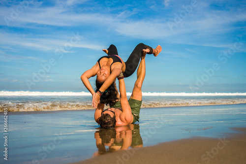 young attractive and concentrated couple of acrobats practicing acro yoga balance and meditation exercise on beautiful beach under a blue sky in mind and body control photo