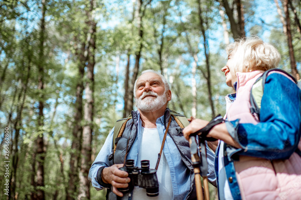 Senior couple looking with binoculars while hiking in the forest. Concept of an active lifestyle on retirement Senior couple looking with binoculars while hiking in the forest. Concept of an active lifestyle on retirement