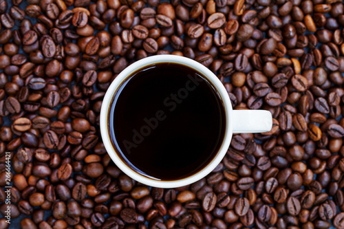 Black coffee in white cup on freshly roasted coffee beans background. Top view. Copy space.