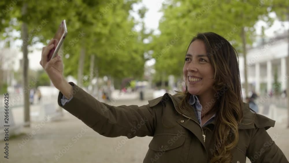 Smiling young woman taking selfie with smartphone outdoor. Attractive young lady with long hair taking pictures with modern phone during sunny day. Technology concept Smiling young woman taking selfie with smartphone outdoor. Attractive young lady with long hair taking pictures with modern phone during sunny day. Technology concept