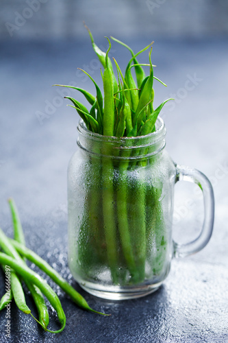 Green beans in glass jar on grey stone background.