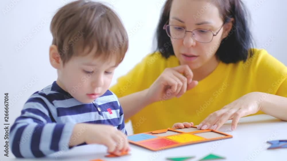 little asian boy collects puzzles with mom sitting at the desk. A cute child collects a picture from large multi-colored details. Playing with a puzzle. slow motion. Teacher playing with boy little asian boy collects puzzles with mom sitting at the desk. A cute child collects a picture from large multi-colored details. Playing with a puzzle. slow motion. Teacher playing with boy