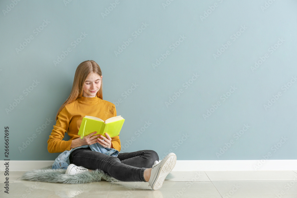 Cute teenage girl with book sitting on floor near color wall Cute teenage girl with book sitting on floor near color wall