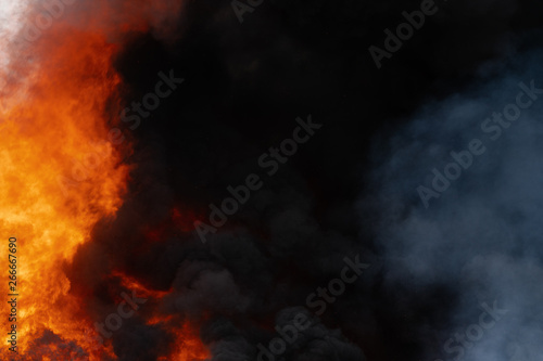 Dangerous huge flames of red fire, motion blur clouds of dark smoke covered sky. Defocus, haze from strong fire and high temperature from flames. Atmospheric and smoke dispersion.