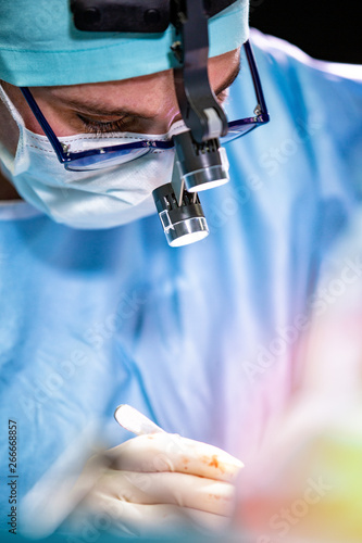 Surgeon performing surgery in hospital operating room. Surgeon in mask wearing loupes during medical procadure.