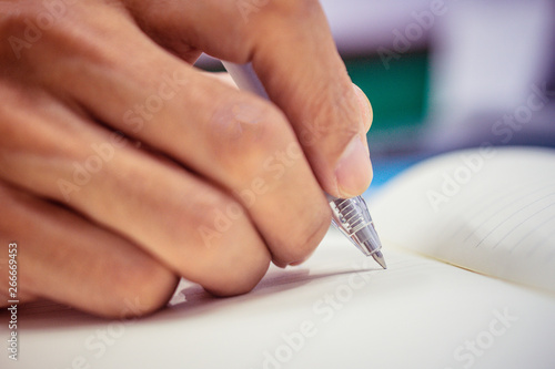 Hand holding pen and writing on book