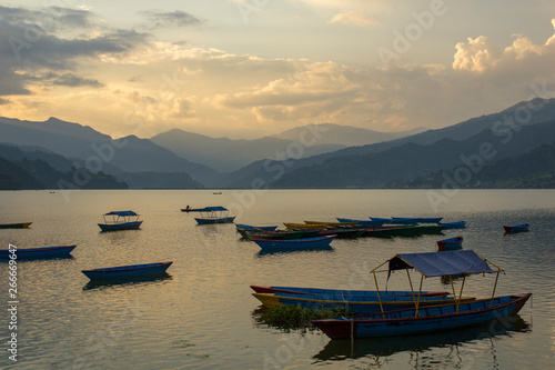 wooden old empty blue boats on the lake Phewa on the background of a mountain valley in the fog and the evening sky © Pavel