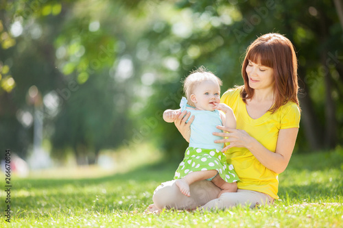 Happy mother and daughter in the summer park. Beauty nature scene with family outdoor lifestyle. Happy family resting together on the green grass, having fun outdoor. Happiness and harmony