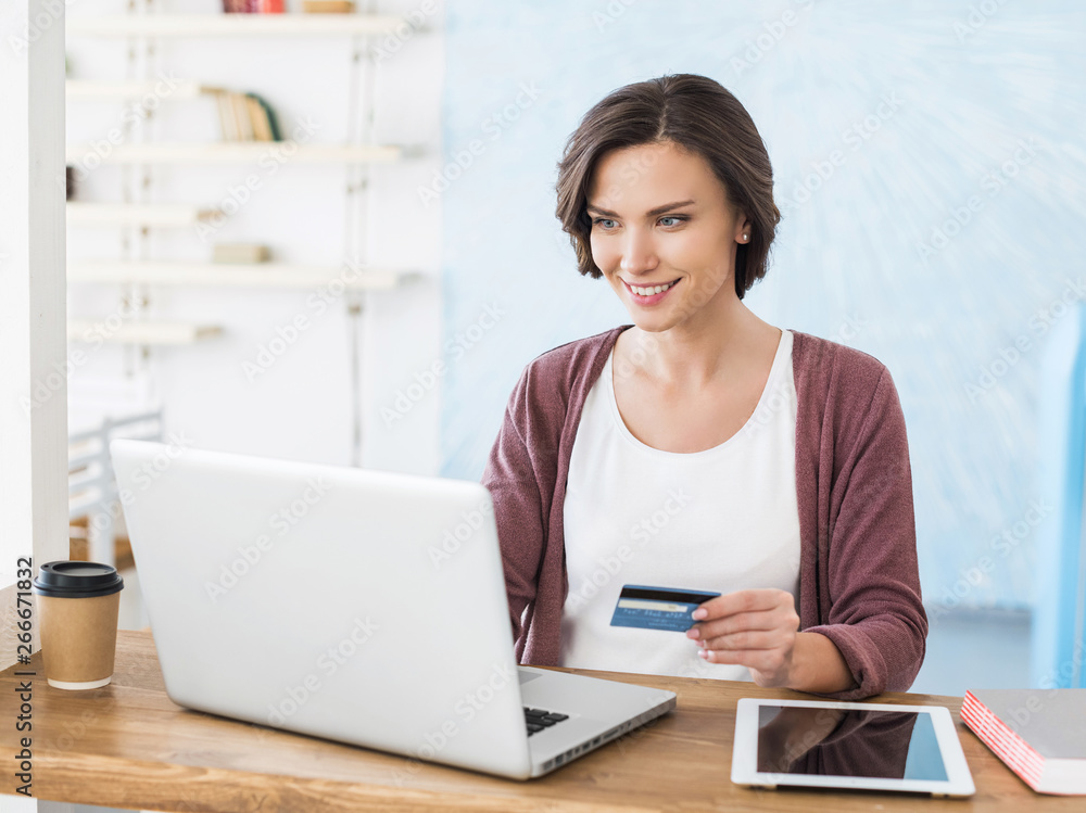 Young woman using laptop computer and holding credit card. Businesswoman or entrepreneur working. Online shopping, e-commerce, spending money, enjoying life concepts Young woman using laptop computer and holding credit card. Businesswoman or entrepreneur working. Online shopping, e-commerce, spending money, enjoying life concepts