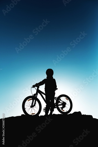 Silhouette of a little girl with a bicycle at sunset