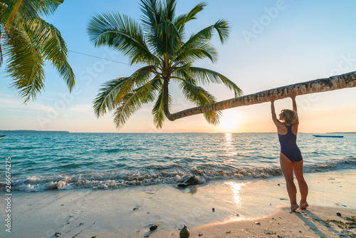 Woman relaxing under coconut palm frond on scenic white sand beach, sunny day, turquoise transparent water, real people. Indonesia, Kei islands, Moluccas Maluku, Wab beach
