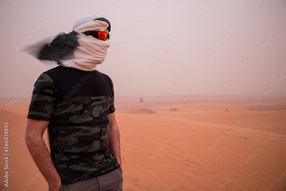 A man with his head covered by a headscarf and sunglasses during a sandstorm in the desert A man with his head covered by a headscarf and sunglasses during a sandstorm in the desert