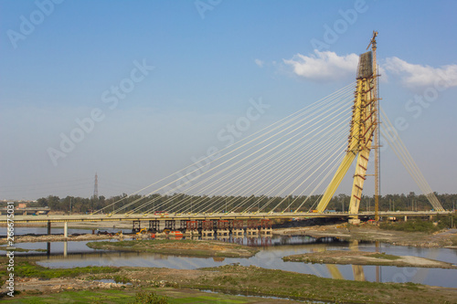 cable-stayed bridge under construction and a tower crane over the Yamuna River against a blue sky. Signature Bridge. Delhi India