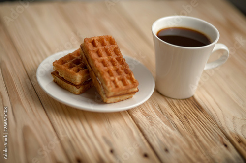 Hot coffee on a wooden stand with waffle, top view