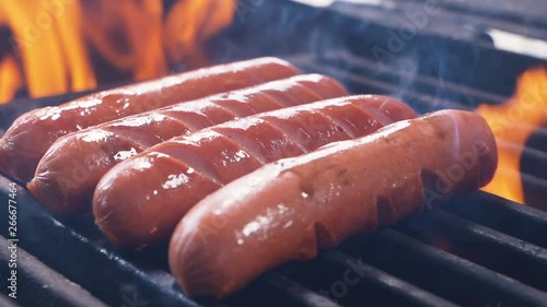 Prepare few sausages and hot dogs On The Hot Flaming BBQ Charcoal Grill. Classic Takeaway Meal. Street food cooked on hot plate. Close up Slow motion