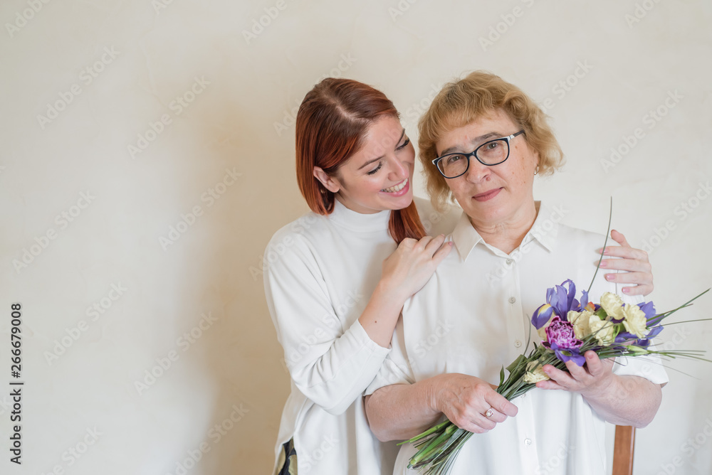 Daughter giving flowers to adult mother. Daughter gives flowers to her mother and hugs her. Spending time together, celebrating at home on weekends. Mothers Day Daughter giving flowers to adult mother. Daughter gives flowers to her mother and hugs her. Spending time together, celebrating at home on weekends. Mothers Day