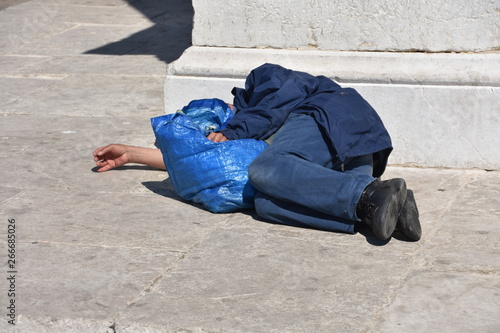 A homeless man sleeps in the street in broad daylight