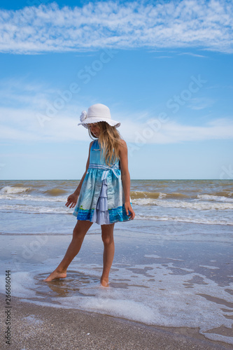 Beautiful seascape. The girl the blonde in a blue dress and a white hat in hand walks along the shore