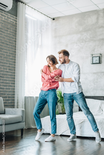 happy woman dancing with handsome bearded man in bedroom