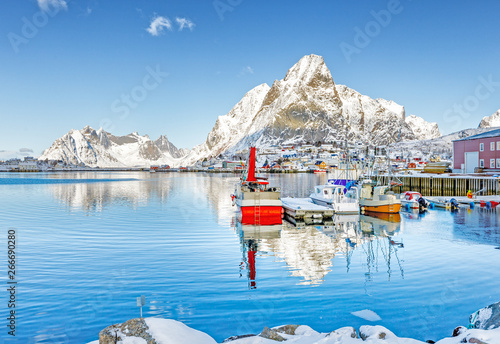 Spectacular view of arctic village at picturesque snow capped mountain peaks background in sunny winter day. Lacation Reine village on Lofoten Islands in Norway, Scandinavia. photo