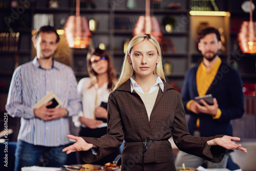 Young serious blonde Caucasian businesswoman sredded elegant posing with her successful team in restaurant.