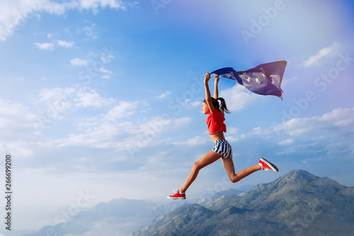 Child teenager girl jumping on the top of the mountain with an European Union flag on her shoulders. Sunset time