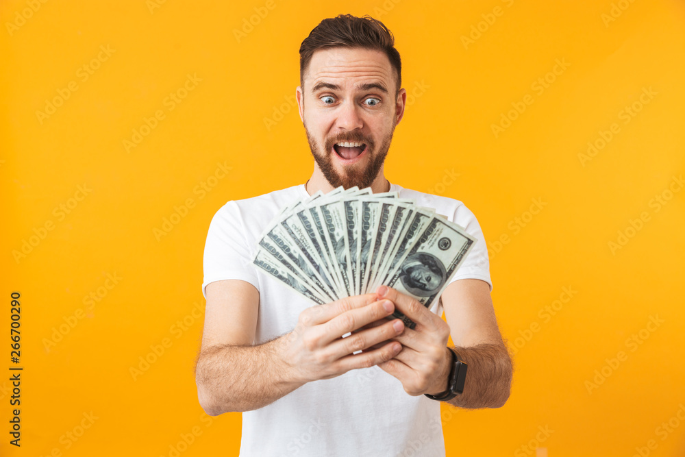 Excited man posing isolated over yellow wall background holding money. Excited man posing isolated over yellow wall background holding money.